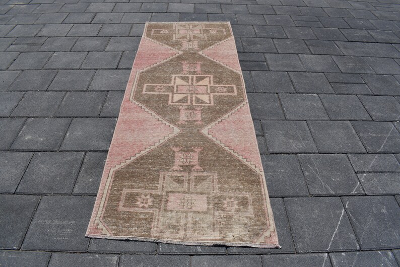 May include: A long, rectangular rug with a pink and brown geometric pattern. The rug has a distressed, vintage look.