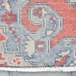 May include: A vintage rug with a geometric pattern in shades of red, blue, and white. The rug has a fringe border.