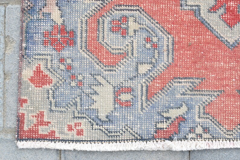 May include: A vintage rug with a geometric pattern in shades of red, blue, and white. The rug has a fringe border.