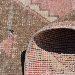 May include: Close-up of a woven rug with a pink and brown geometric pattern. The rug is folded over, showing the underside of the weave.