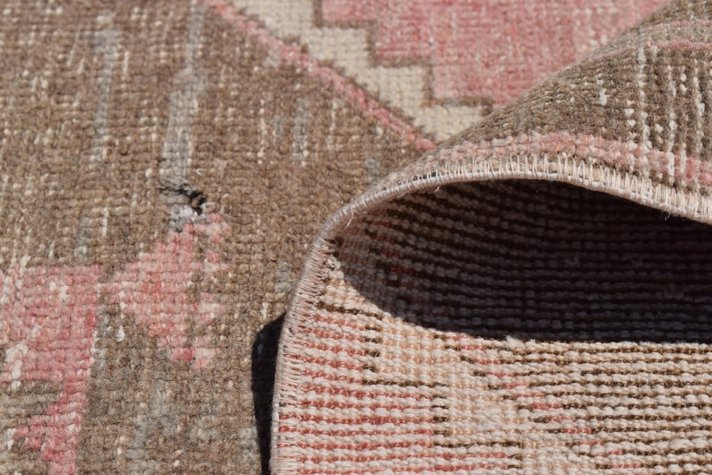 May include: Close-up of a woven rug with a pink and brown geometric pattern. The rug is folded over, showing the underside of the weave.