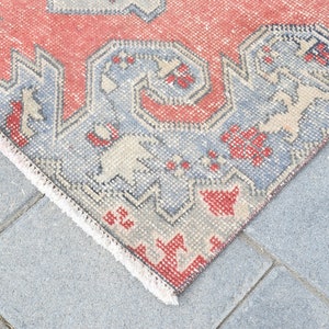 May include: Close-up of the edge of a red and blue patterned rug with a white fringe. The rug is lying on a gray concrete surface.