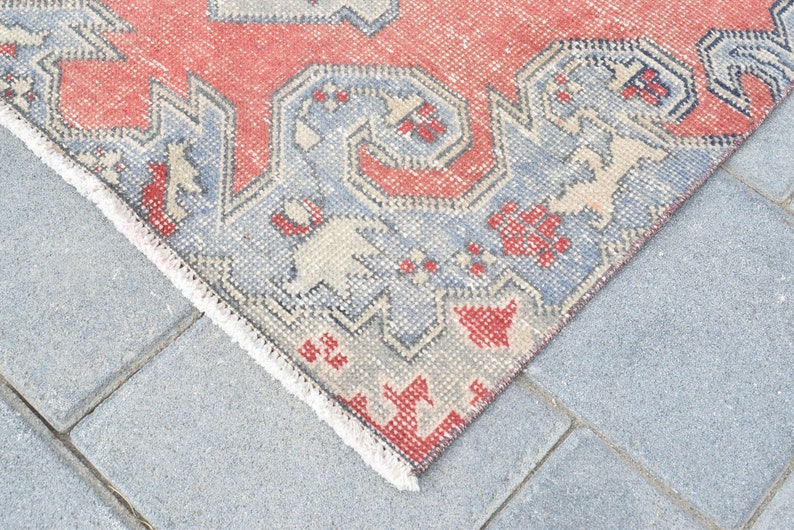 May include: Close-up of the edge of a red and blue patterned rug with a white fringe. The rug is lying on a gray concrete surface.