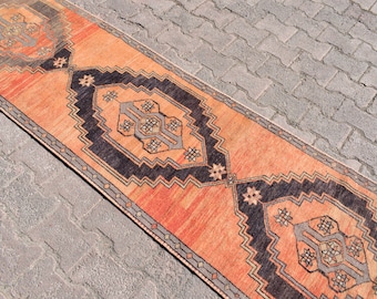 Peut inclure: Un tapis long et étroit avec un motif persan traditionnel. Le tapis est un mélange de couleurs orange, noir et gris. Le tapis est posé sur une surface en briques grises.