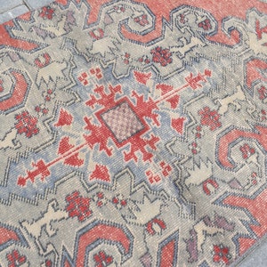 May include: A vintage rug with a geometric pattern in shades of red, blue, and white. The rug has a distressed look, with faded colors and a worn texture.