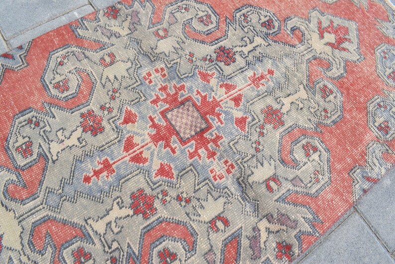 May include: A vintage rug with a geometric pattern in shades of red, blue, and white. The rug has a distressed look, with faded colors and a worn texture.