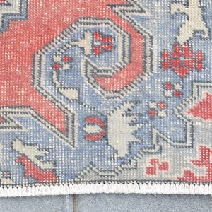 May include: Close-up of a red, blue, and white patterned rug with a fringe border. The rug has a traditional design with geometric shapes and floral motifs.