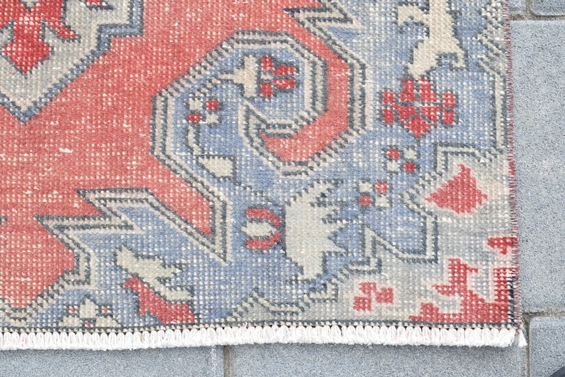 May include: Close-up of a red, blue, and white patterned rug with a fringe border. The rug has a traditional design with geometric shapes and floral motifs.