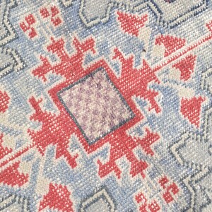 May include: A close-up of a blue and red patterned rug with a geometric design. The rug has a faded, vintage look.