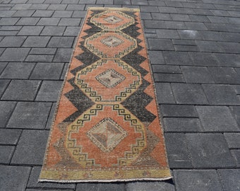 Può includere: Un tappeto lungo e stretto con un motivo geometrico in tonalità arancio, nero e beige. Il tappeto ha un design tradizionale con forme di diamante ripetute e bordi intricati.