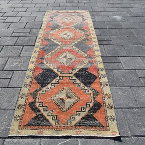 Op de afbeelding: Een vintage Turkse loper met een geometrisch patroon in tinten rood, zwart en crème. De loper heeft een verweerde look en is perfect om een ​​bohemien touch aan je huis toe te voegen.