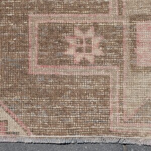 May include: Close-up of a brown and pink patterned rug with a fringe border. The rug has a geometric design with a central motif.