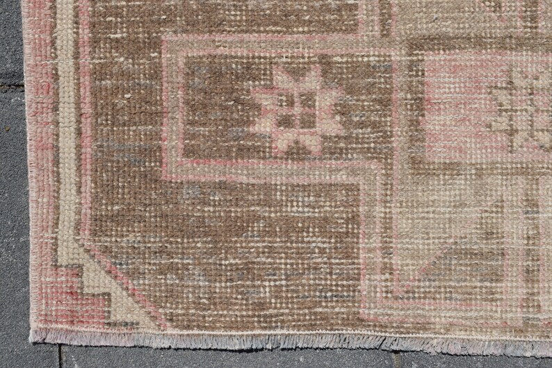 May include: Close-up of a brown and pink patterned rug with a fringe border. The rug has a geometric design with a central motif.