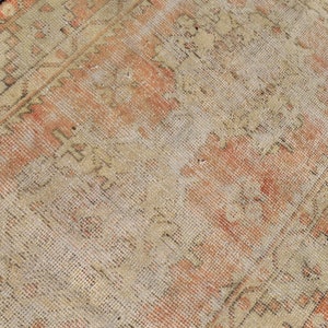 Op de afbeelding: Een vintage tapijt met een vervaagde oranje en crème kleurstelling. Het tapijt heeft een traditioneel Perzisch ontwerp met ingewikkelde bloemmotieven.