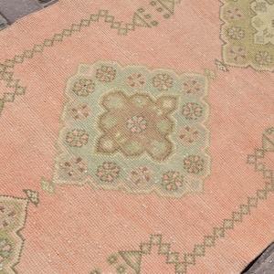 Könnte beinhalten: Ein rosafarbener und grüner Teppich mit einem floralen Muster. Der Teppich hat einen abgenutzten Look und ist aus einem weichen, gewebten Material gefertigt.