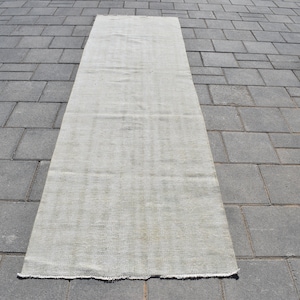 May include: A long, off-white, rectangular rug with a woven texture. The rug is lying flat on a grey concrete surface.