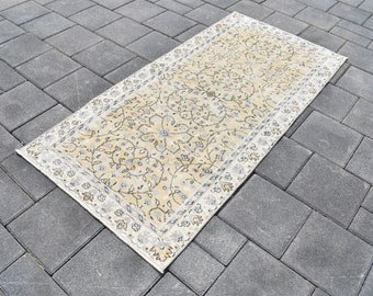 May include: A rectangular rug with a cream-colored central field and a floral pattern in shades of beige and gray. The rug has a decorative border and is placed on a gray brick surface.