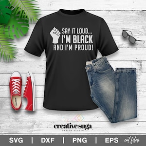 Può includere: Maglietta nera con un grafico di pugno alzato e il testo "SAY IT LOUD... I'M BLACK AND I'M PROUD!"