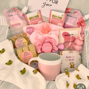 Può includere: Una confezione regalo rosa piena di articoli per la cura di sé. Include una tazza rosa, calzini con orsetti, maschere per il viso, bustine di tè, una fascia per capelli, scrub per le labbra e una carta con "JUST FOR YOU" e "Mama BEAR".