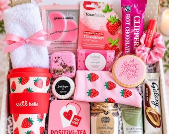 May include: A gift box containing a white towel with a pink ribbon, pink eye masks, a strawberry sheet mask, a hot chocolate packet, a lip balm, a strawberry-patterned cup, a bath bomb, a soap bar, strawberry socks, a cookie, a candle, and chocolate.