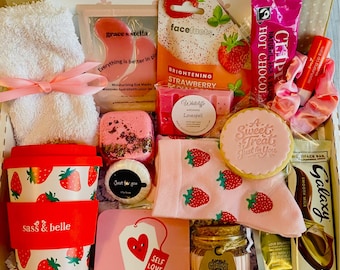 May include: A gift box filled with self-care items. Includes a white towel tied with a pink ribbon, strawberry-themed tumbler and socks, face masks, a cookie, lip balm, a candle, and a bar of chocolate. The box has the text "A little something to brighten your day..."