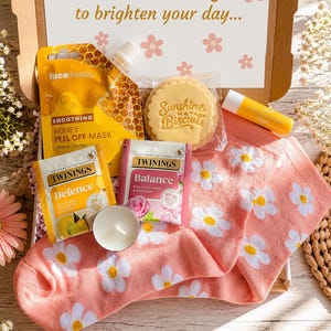 以下が含まれることがあります： Face Factsのハニーピールオフマスク、Sunshine in a Biscuitクッキー、レモンリップバーム、TwiningsのDefenceとBalanceティーバッグ、小さな白いティーライトキャンドル、そして白いデイジー柄のピンクの靴下が入ったギフトボックス。