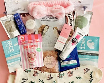 May include: A gift box filled with self-care items for a new or expecting parent. Includes a pink headband, face masks, hand cream, candy, socks with floral embroidery, and other beauty products. The box is on a pink surface.