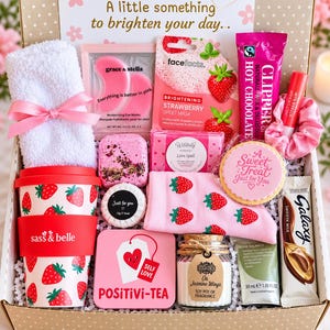 Può includere: Una scatola regalo contenente un asciugamano bianco con nastro rosa, maschere per occhi rosa, una maschera in tessuto alla fragola, una bustina di cioccolata calda, balsamo labbra, una tazza con motivo a fragole, una bomba da bagno e cioccolato.