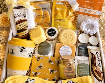 May include: A gift box containing a white towel with a yellow ribbon, Galaxy hot chocolate, eye masks, honey peel-off mask, Vitamin C sheet mask, a white scrunchie, two tea lights, a bee-patterned travel mug, a bee coaster, and yellow bee socks.