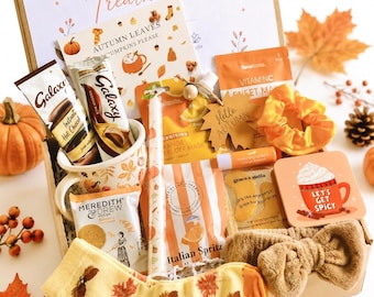 May include: A gift box labeled Welcome to your Treathamper containing a mug, Galaxy hot chocolate, Meredith & Drew biscuits, a candle, orange face mask, eye masks, lip balm, a scrunchie, a headband, and socks with an autumn leaf pattern.