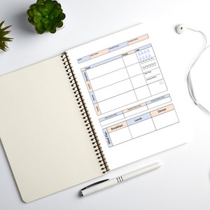 May include: A white spiral bound notebook with a meal plan and activity tracker. The notebook has a light peach and light blue color scheme. The notebook is open to a page with a meal plan section and an activity tracker section. The activity tracker section has a log with water drops and heart icons.