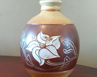 May include: A brown and tan ceramic vase with a white floral design. The vase has a rounded body and a narrow neck.