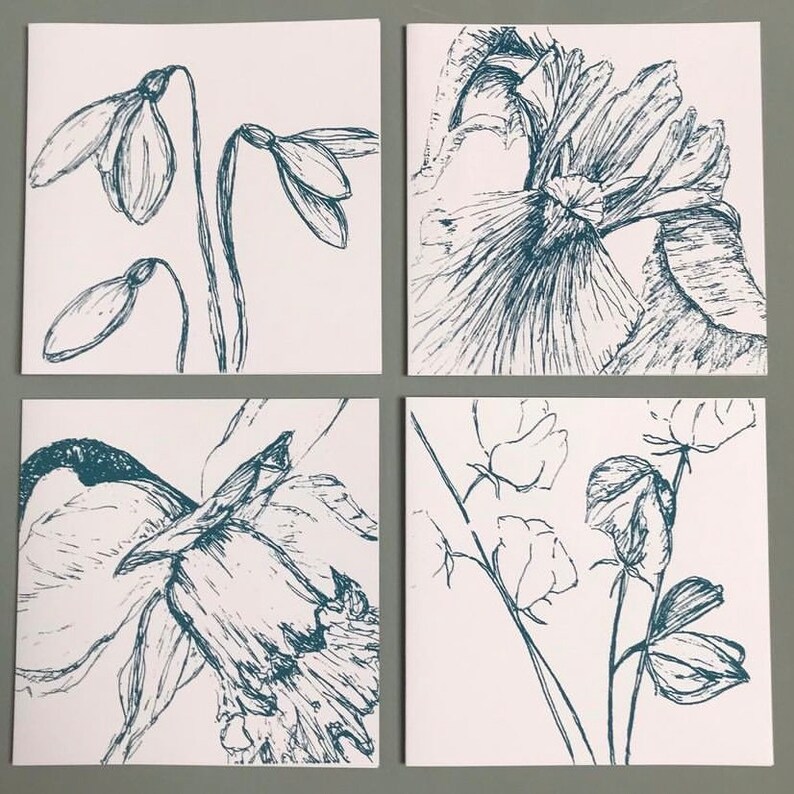 May include: Set of four greeting cards featuring hand-drawn illustrations of flowers in a blue ink. The cards feature a snowdrop, a daffodil, a sweet pea, and a large flower with a ruffled center.