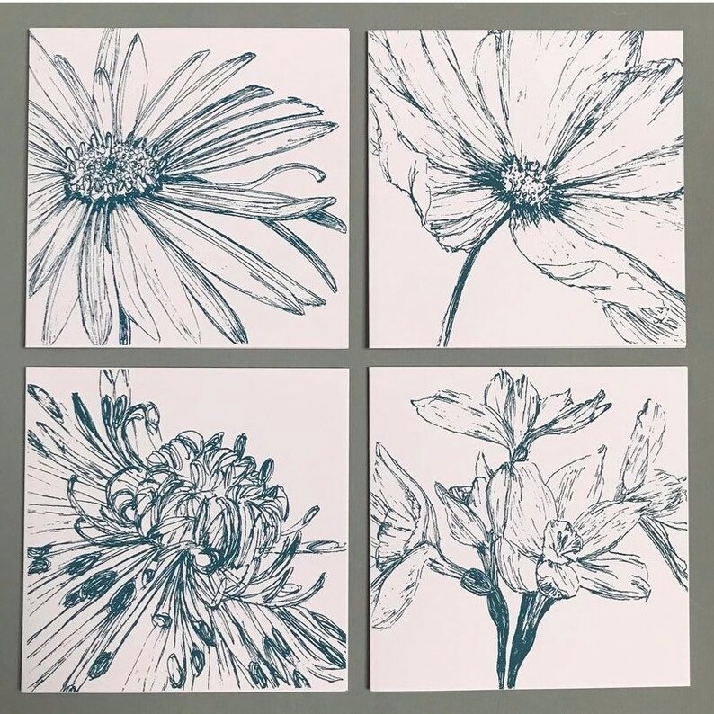 May include: Four square tiles with black and white line drawings of flowers. The tiles feature a daisy, a cosmos, a chrysanthemum, and a daffodil.