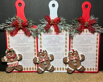 May include: Three decorative cutting boards with red and white handles. Each board features a gingerbread man and a recipe for "Old Fashioned Gingerbread Men." The boards are adorned with festive bows and greenery.