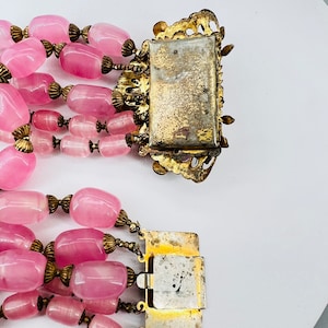Puede incluir: Un collar de cuentas de vidrio rosa de m&uacute;ltiples hilos con cierres y detalles de metal dorado. El collar tiene un aspecto vintage y est&aacute; hecho de m&uacute;ltiples hilos de cuentas de vidrio rosa.