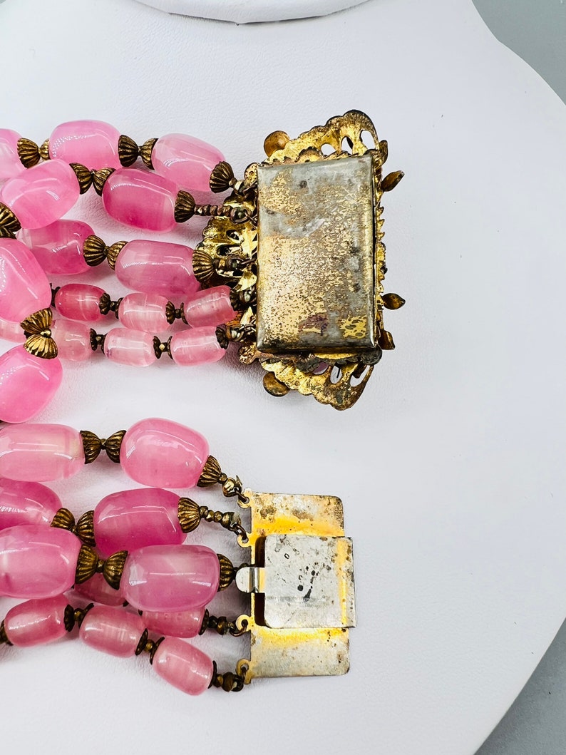Puede incluir: Un collar de cuentas de vidrio rosa de m&uacute;ltiples hilos con cierres y detalles de metal dorado. El collar tiene un aspecto vintage y est&aacute; hecho de m&uacute;ltiples hilos de cuentas de vidrio rosa.