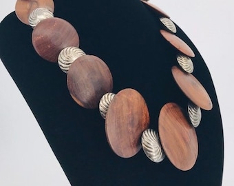 Peut inclure: Un collier ras du cou imposant composé de grosses perles rondes en bois avec des accents argentés. Les perles sont d'une couleur brun foncé et présentent un grain de bois naturel.