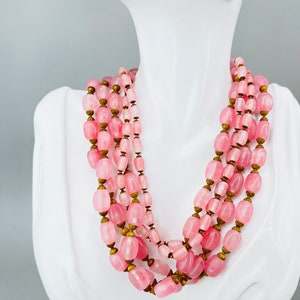 Puede incluir: Un collar de m&uacute;ltiples hilos hecho de cuentas ovaladas de color rosa con detalles dorados. El collar se muestra en un maniqu&iacute; blanco.