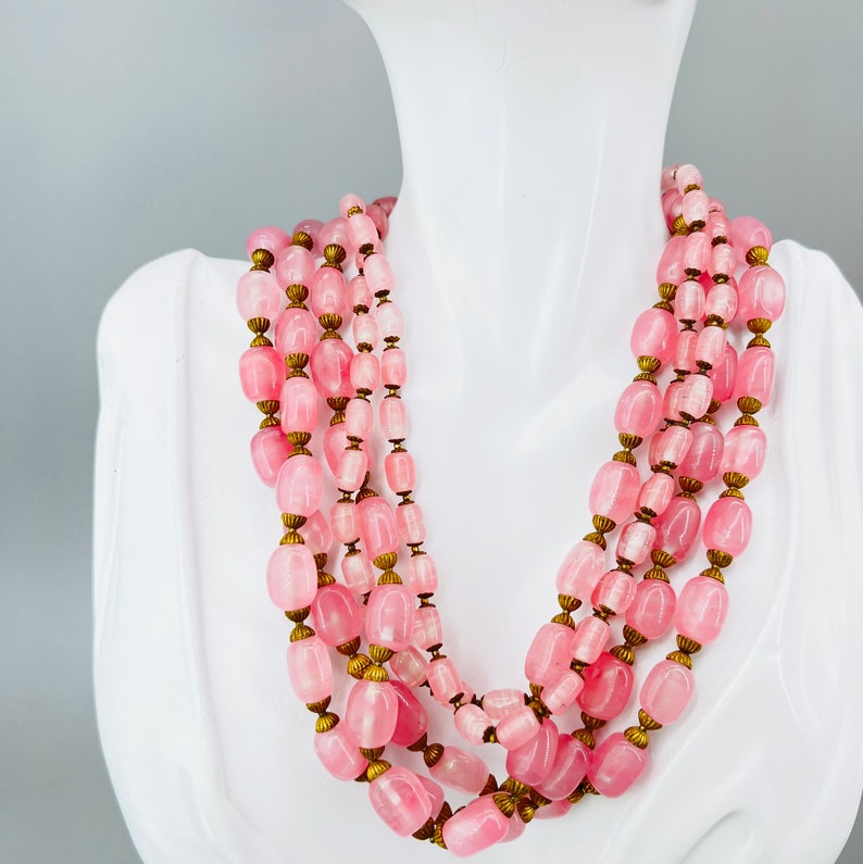 Puede incluir: Un collar de m&uacute;ltiples hilos hecho de cuentas ovaladas de color rosa con detalles dorados. El collar se muestra en un maniqu&iacute; blanco.