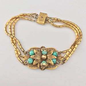 May include: A gold bracelet with a floral design and turquoise stones. The bracelet is made of multiple strands of small gold beads.