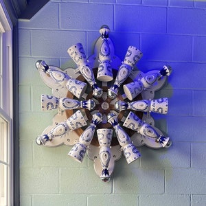 May include: A white and blue ceramic wall art piece with a circular design. The piece features 12 small, decorative bottles arranged in a circular pattern. The bottles are painted with blue and white floral designs.
