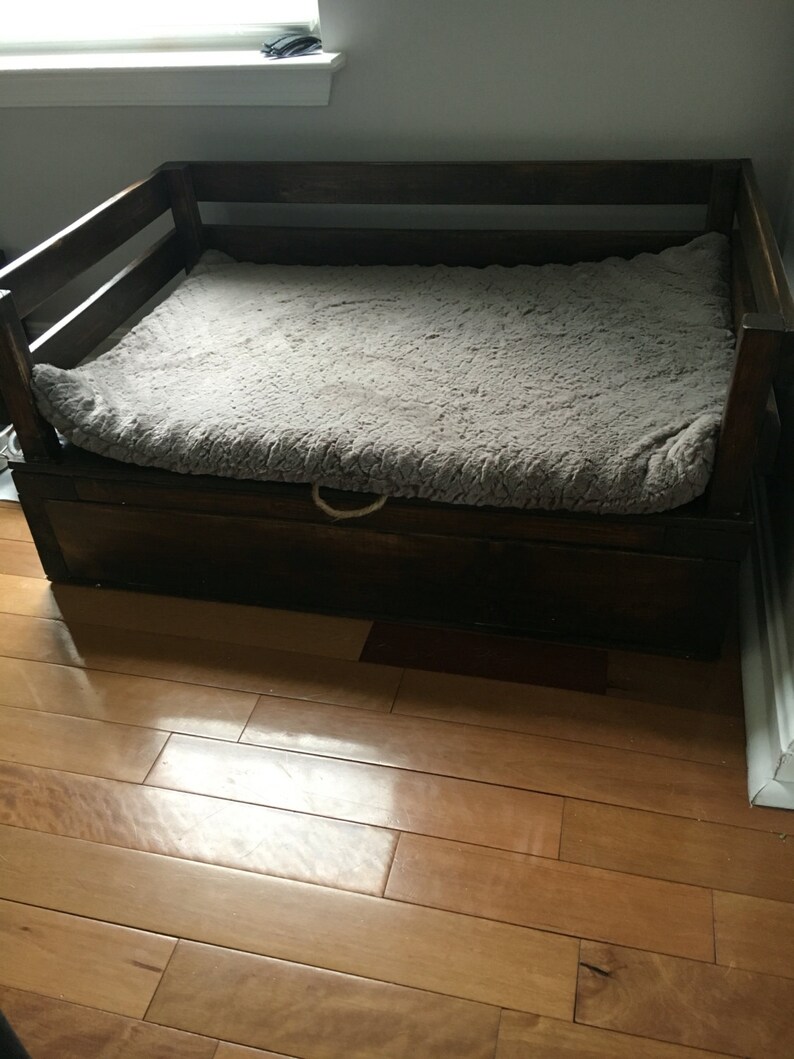 May include: A dark brown wooden dog bed with a gray faux fur mattress and a storage drawer underneath.