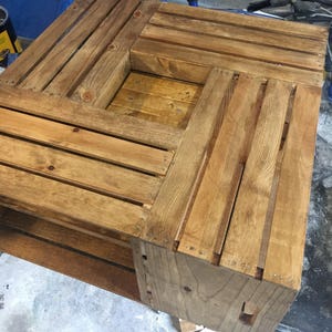 Op de afbeelding: Een houten salontafel gemaakt van hergebruikte kratten. De tafel heeft een vierkant blad en een onderplank. Het hout is in een lichte bruine kleur gebeitst.