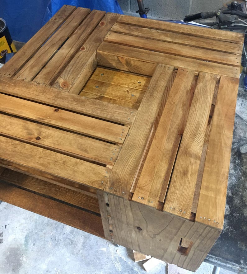 Op de afbeelding: Een houten salontafel gemaakt van hergebruikte kratten. De tafel heeft een vierkant blad en een onderplank. Het hout is in een lichte bruine kleur gebeitst.