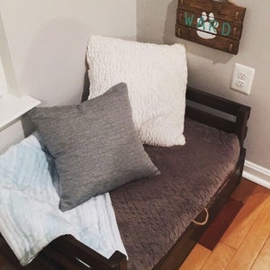 May include: A wooden dog bed with a brown and gray blanket, a gray pillow, and a white pillow. The bed has a drawer and a sign that says "WARD" with a paw print.