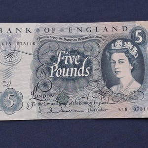 May include: A Bank of England five-pound note featuring a portrait of Queen Elizabeth II. The note has the text "Five Pounds" prominently displayed, along with the bank's name and other details. The note is light blue and white.