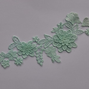 May include: A detailed mint-green floral lace applique. The design includes several flowers of different sizes, leaves, and other decorative elements. The lace is intricately detailed, with a soft, textured appearance. Suitable for embellishing garments or craft projects.
