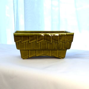 以下が含まれることがあります： 幾何学模様の緑色のセラミック製のプランター。プランターは正方形で、わずかに盛り上がった縁と4本の小さな足があります。