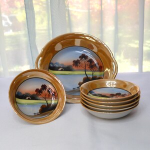 May include: Set of five vintage Japanese porcelain bowls with a gold rim and hand-painted landscape scenes. The bowls feature a light blue background with brown trees and a white house.